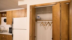 Une cuisine avec des meubles de rangement en bois, un réfrigérateur blanc et un étendoir suspendu où sont accrochés des vêtements.