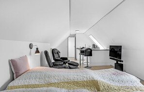 Cozy retreat with a neatly made bed, black leather chair, and mounted TV.