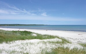 Een strand met wit zand en helderblauw water. Mensen wandelen langs de kust.