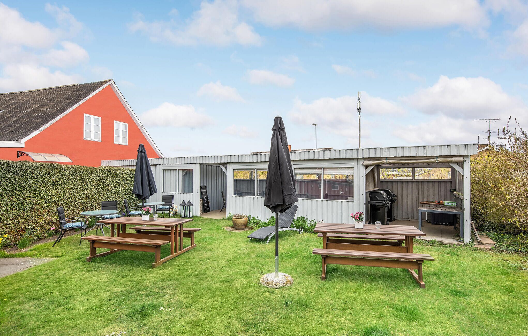 A backyard with two wooden picnic tables, a barbecue grill, and a shed.