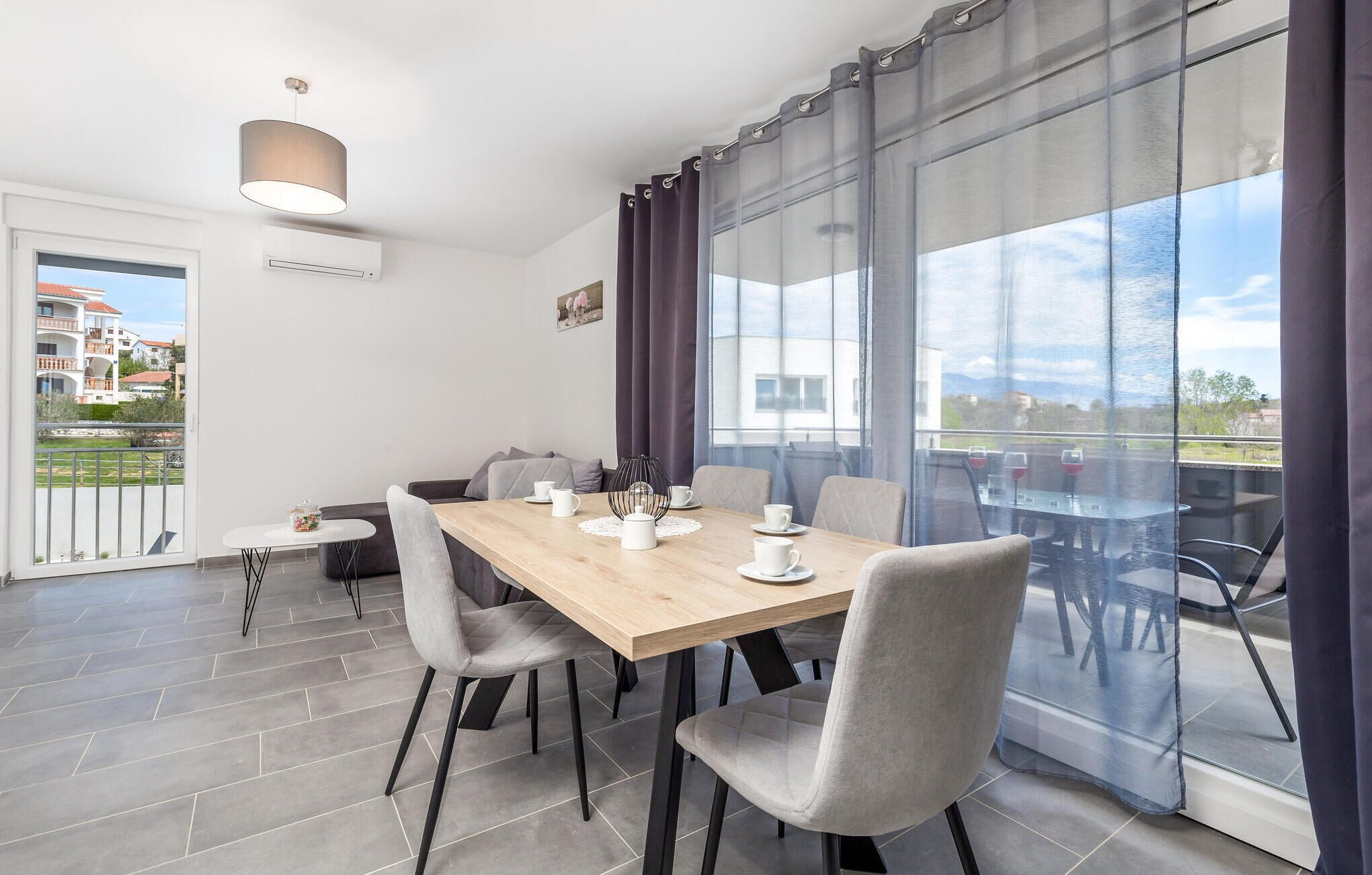 Een moderne eetruimte met een houten tafel, grijs gestoffeerde stoelen en uitzicht op de stad door grote ramen.