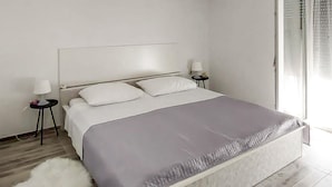 Una camera da letto moderna con un letto, due comodini, un tappeto bianco e vista sull'esterno.