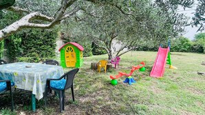 Un giardino con una piccola casetta per bambini, uno scivolo e un tavolo con sedie.