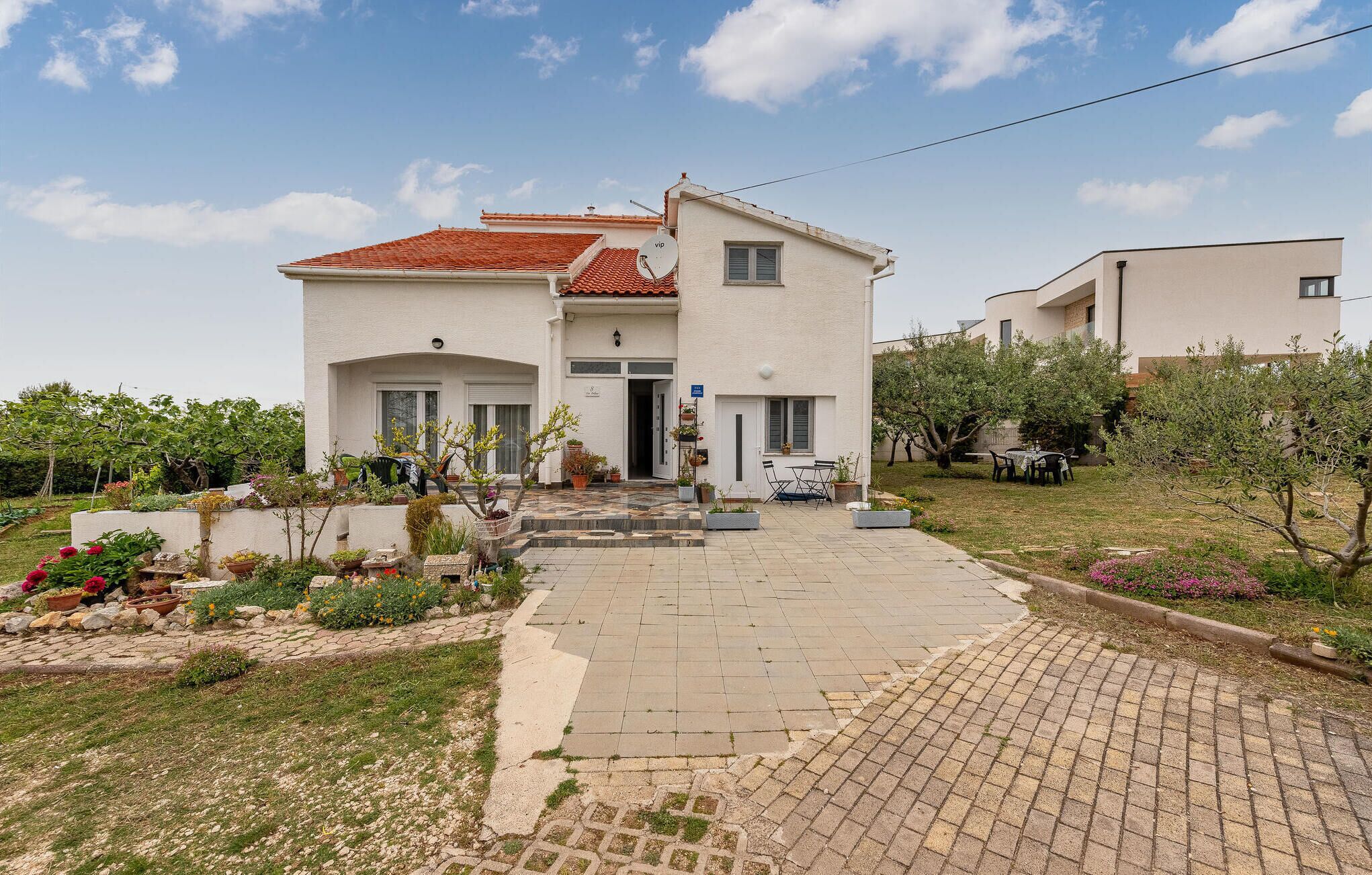A two-story house with a tiled roof, a paved driveway, and a garden with various plants and flowers.