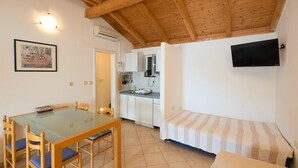 Een ruimtelijk ingerichte leefruimte met een eethoek, kitchenette en een bed.