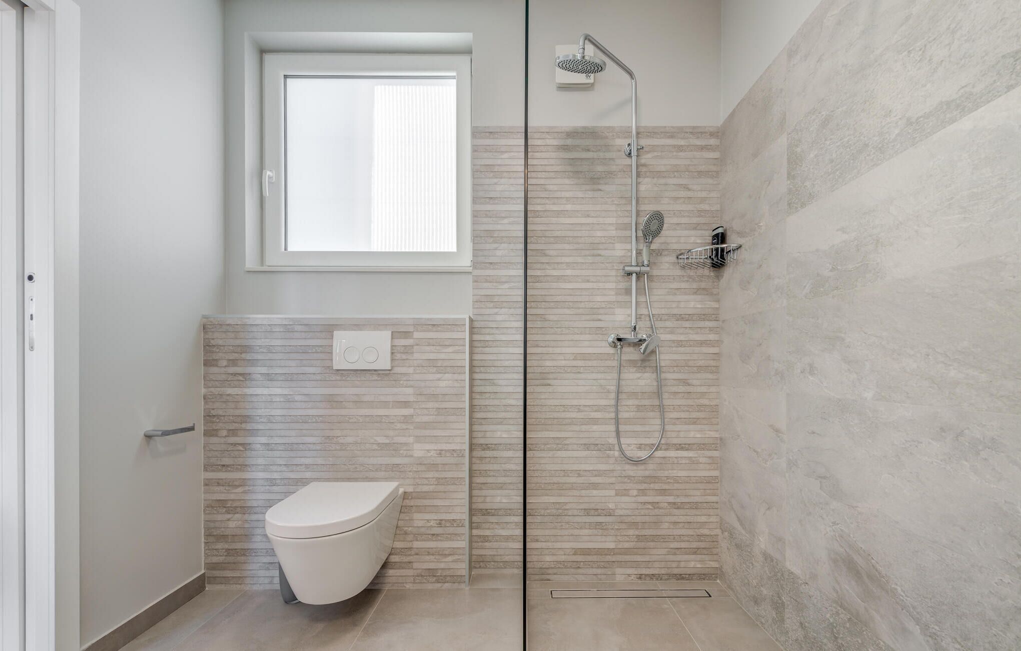 Ein modernes Badezimmer mit Bodendusche, Toilette und Fenster.