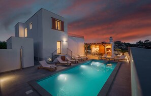 Une maison moderne dotée d’une piscine, d’un espace salon extérieur et d’une cheminée.