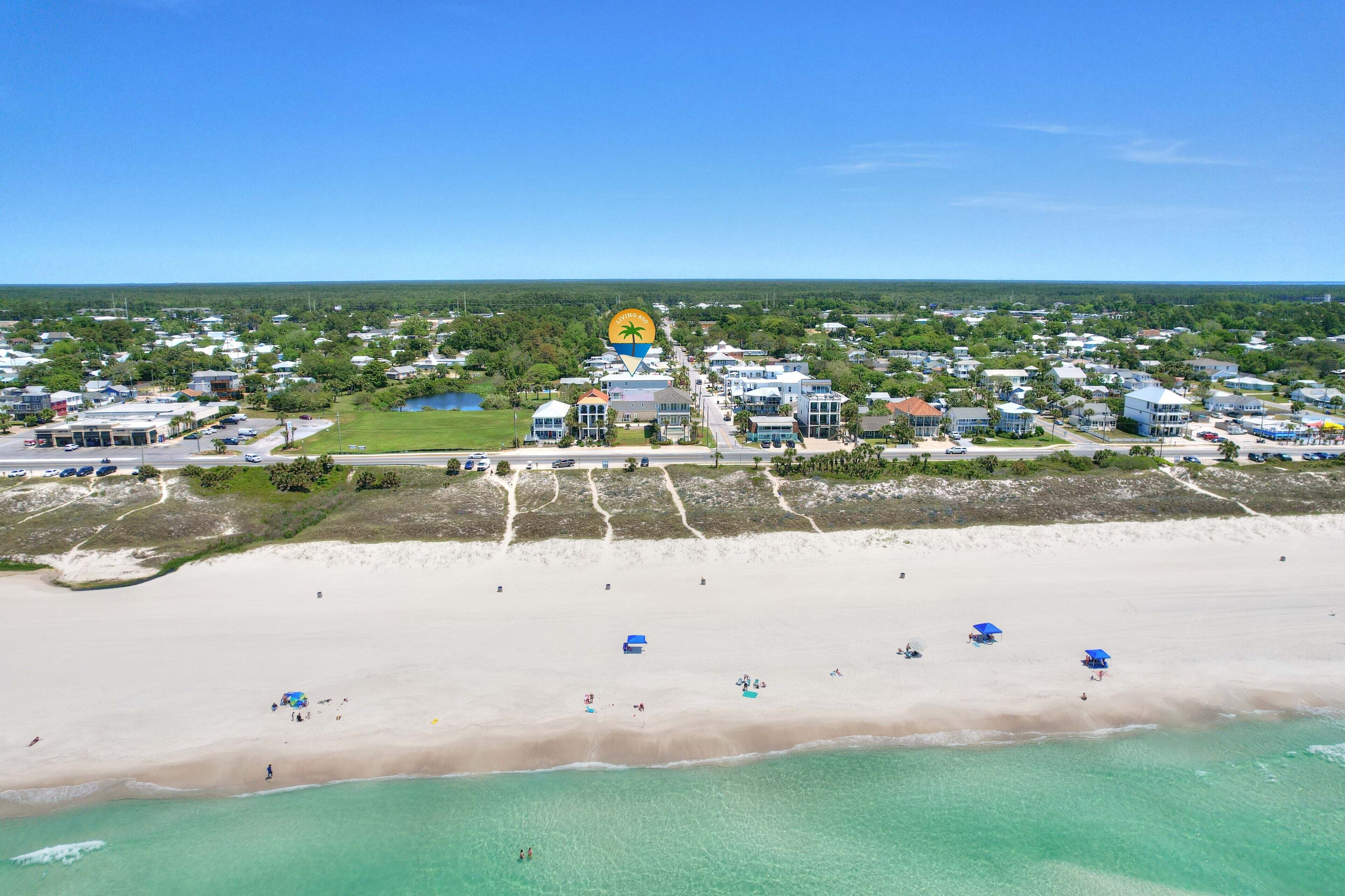 A coastal town with a beach, houses, and a prominent yellow building with a palm tree logo.