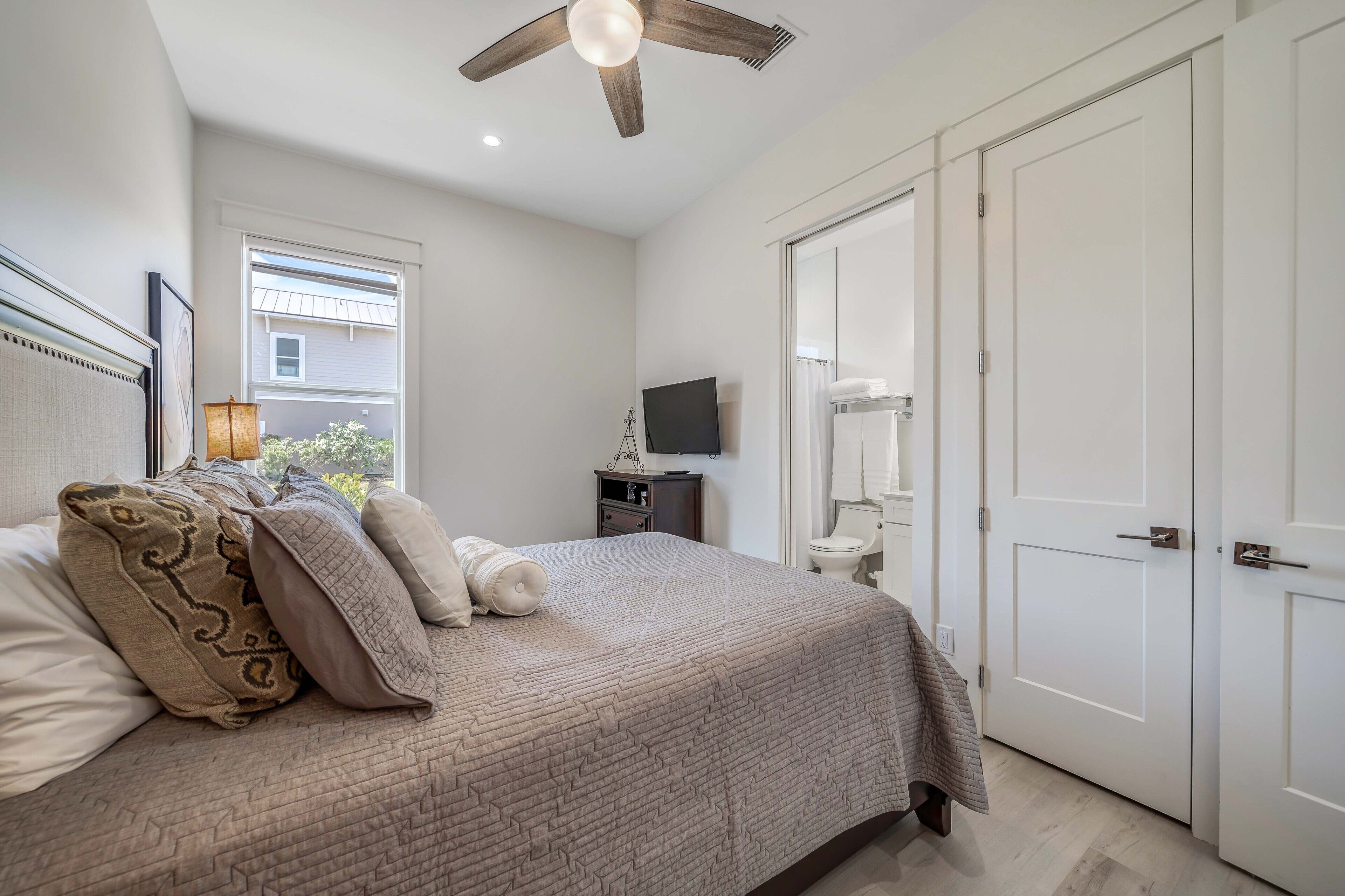 A bedroom with a bed, a ceiling fan, a window, a TV, and a wardrobe.