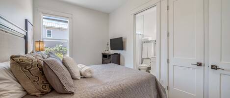 A bedroom with a bed, a ceiling fan, a window, a TV, and a wardrobe.