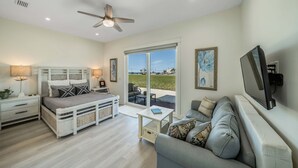 A bedroom with a bed, bedside tables, a ceiling fan, a TV, and a sliding glass door leading to an outdoor area.