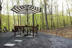 A table with chairs and a striped umbrella in a forested area.