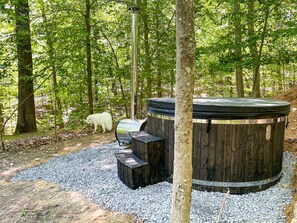 A hot tub surrounded by a wooden deck and gravel, set in a forested area.