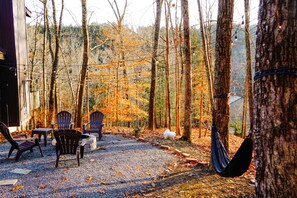 A forested area with a gravel patio, outdoor seating, and a hammock.