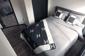 A modern hotel room with a neatly made bed, a dark door, and a view of another room.