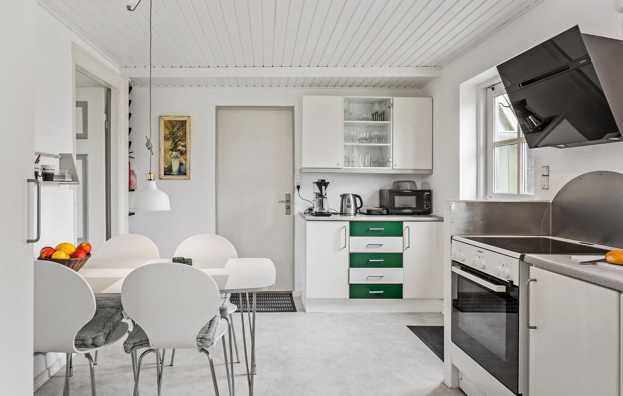 A modern kitchen with white cabinetry, a dining area with white chairs, and a large window.