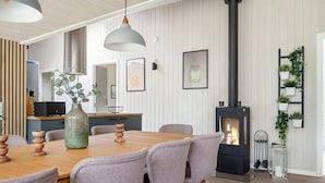 Uma área de jantar moderna com mesa e cadeiras de madeira, uma luminária pendente, uma lareira a lenha preta e um nicho na parede para plantas.