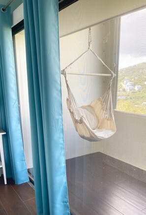 A room with a hanging chair, blue curtains, and a view of buildings through a window.