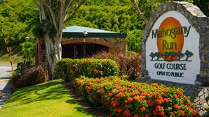A golf course sign with a stone arch and a green roof building in the background. - Updated 1BR/1BA - "Island Sol" with fantastic views (St. Thomas)