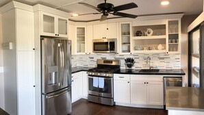 A modern kitchen with stainless steel appliances, white cabinetry, a black countertop, and a ceiling fan. - Updated 1BR/1BA - "Island Sol" with fantastic views (St. Thomas)