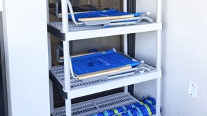 A white storage unit with multiple shelves, including a top shelf with a white container and a lower shelf with blue and green striped bags. - Updated 1BR/1BA - "Island Sol" with fantastic views (St. Thomas)