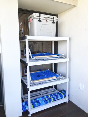 Un meuble de rangement blanc doté de plusieurs étagères, dont une étagère supérieure avec un récipient blanc et une étagère inférieure avec des sacs à rayures bleues et vertes.