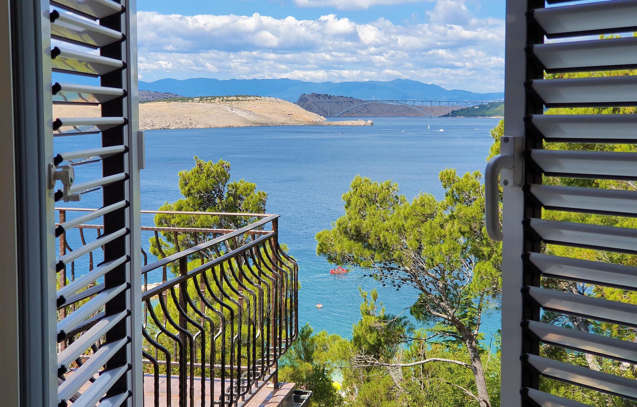 A balcony with a view of a lake, mountains, and a bridge in the distance.
