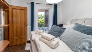 A hotel room with a wooden door, a bed with white and striped bedding, and a view of greenery outside. - Cozy apartment in Jadranovo with house sea view (Jadranovo)