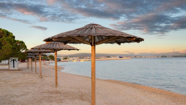 Een strand met verschillende rieten parasols en een zandstrand.
