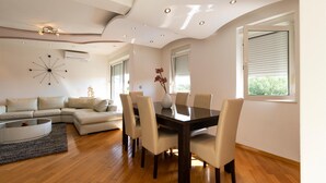 Een moderne woonkamer met een eethoek, met een gebogen plafond, ingebouwde verlichting, een eigentijdse klok en uitzicht op groen buiten.
