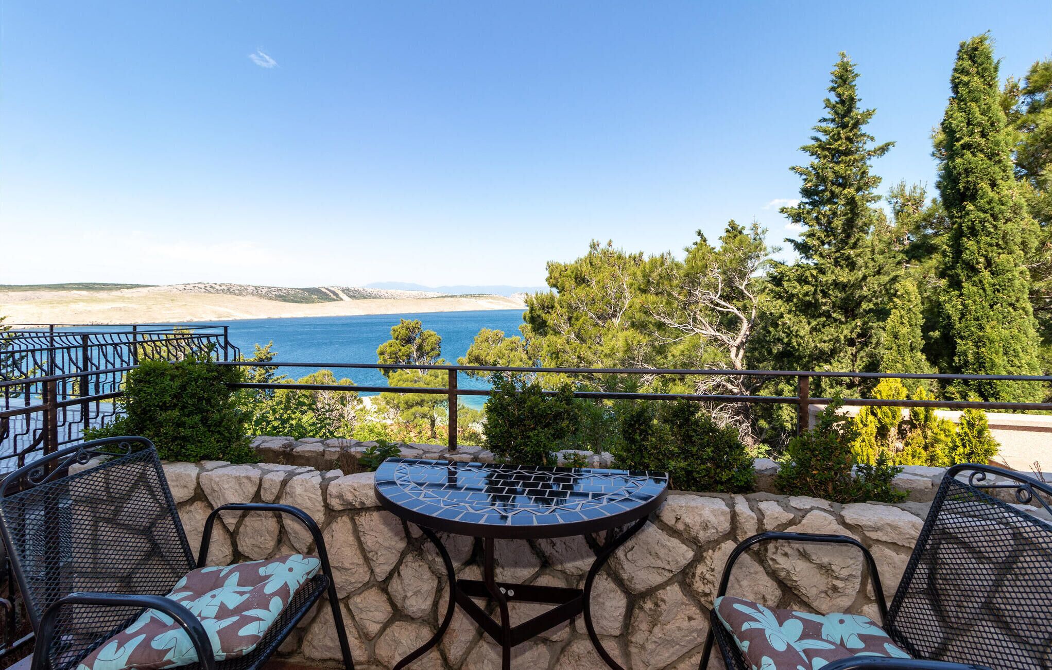 A patio with a table and chairs, overlooking a beach and the sea.