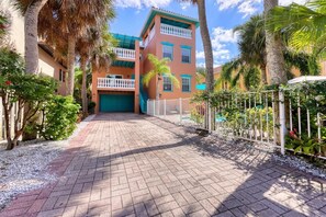 A two-story building with a green garage door, surrounded by a white fence and palm trees.