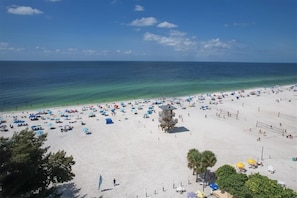 A beach with numerous umbrellas and beach chairs, a lifeguard tower, and clear blue waters.