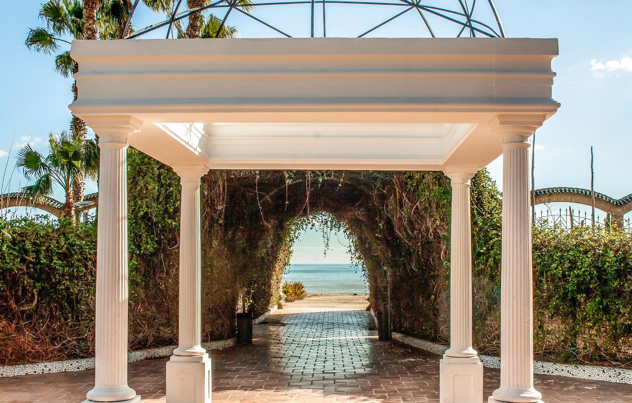Une pergola blanche, ornée de colonnes, qui mène à la plage.