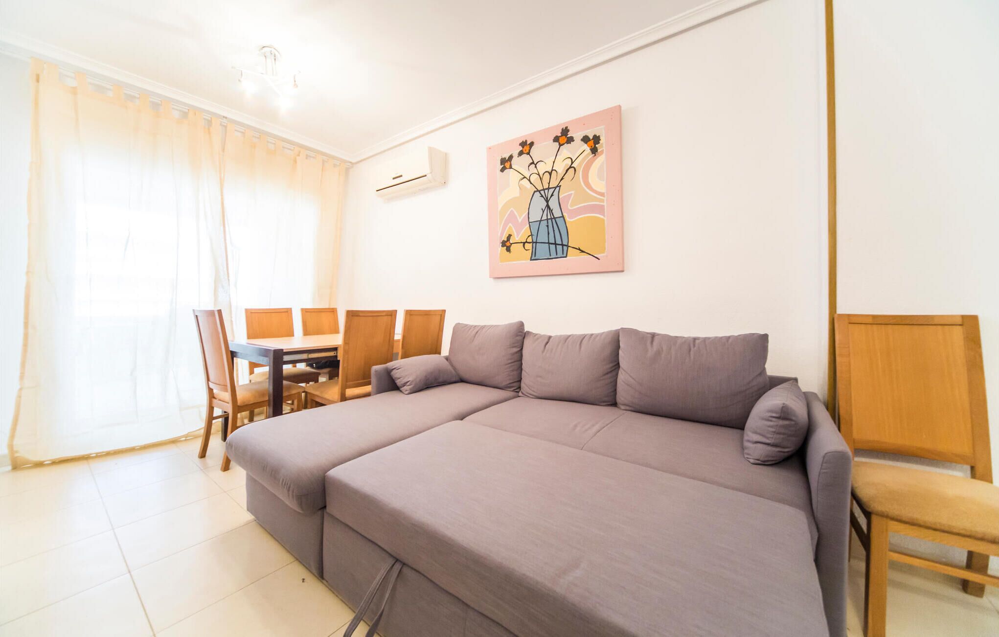 A modern living room with a sofa, a dining table with chairs, and a painting on the wall.