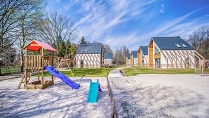 Ein Spielplatz mit Rutsche und Klettergerüst, umgeben von Häusern mit markanter Architektur.