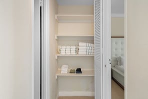 Un dressing accessible sans porte, doté de nombreuses étagères, et un lit visible à travers une porte ouverte.