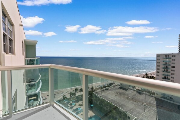A balcony with a clear view of the ocean and a resort area with pools and umbrellas.