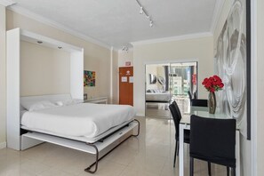 A hotel room with a bed, a dining table with chairs, a vase with flowers, and a large abstract painting on the wall.