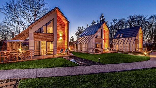 Ein modernes Haus mit zwei großen, dreieckig-gedachten Baukörpern, einem gepflegten Rasen und einem gepflasterten Weg.
