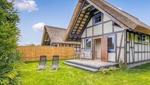 Une maison traditionnelle à colombages, avec un toit de chaume, une clôture en bois et un petit espace extérieur aménagé avec des chaises.