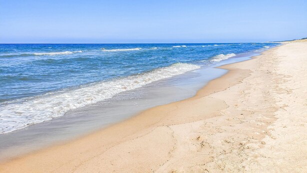 Une plage avec une eau d’un bleu limpide et un rivage sablonneux.
