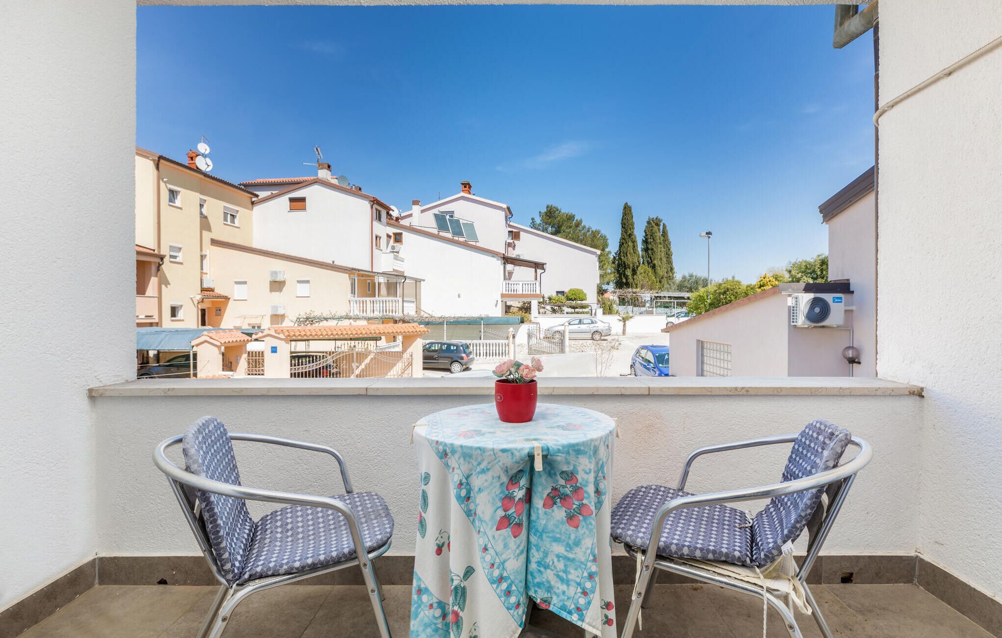 Un balcon avec deux chaises et une table, donnant sur un quartier résidentiel avec des immeubles et des arbres.