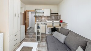 En kompakt opholdsstue med tekøkken, sofa og spiseplads.