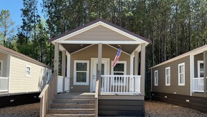 A single-story mobile home with a porch, a flag, and a gravel driveway.