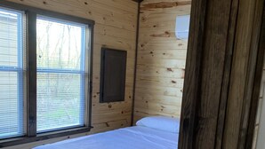 A wooden cabin bedroom with a bed, a window with blinds, and a wooden door.