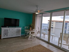 A balcony with a sliding glass door, a dining table with chairs, a white cabinet with decorative cutouts, and a ceiling fan.