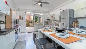 A modern kitchen with white cabinets, a built-in oven, and a refrigerator. There is a dining area with a table set for two, and a view of the outside through an open door. - 1 bedroom gorgeous apartment in Bakar (Bakar)
