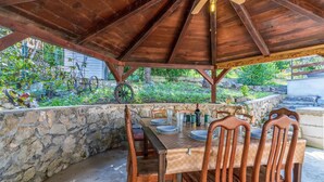 An outdoor wooden pergola dining area with stone walls, wooden chairs, and a table set for four. - 1 bedroom gorgeous apartment in Bakar (Bakar)