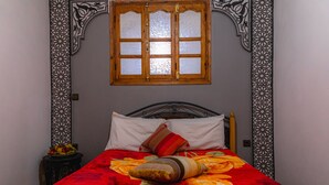Ein Bett mit rotem floralem Überwurf, zwei Kissen und einem Holz-Kopfteil.